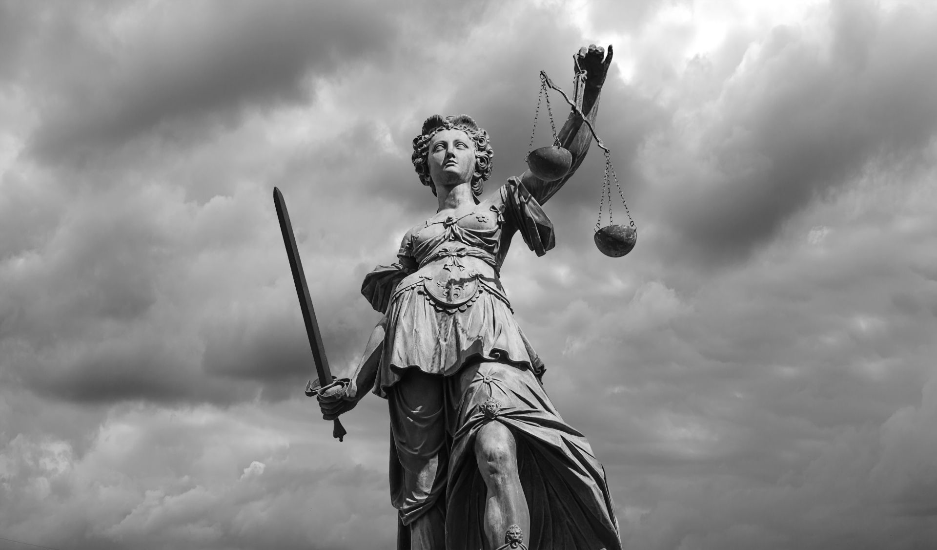 Statue of Lady Justice holding scales and sword, set against a cloudy sky.
