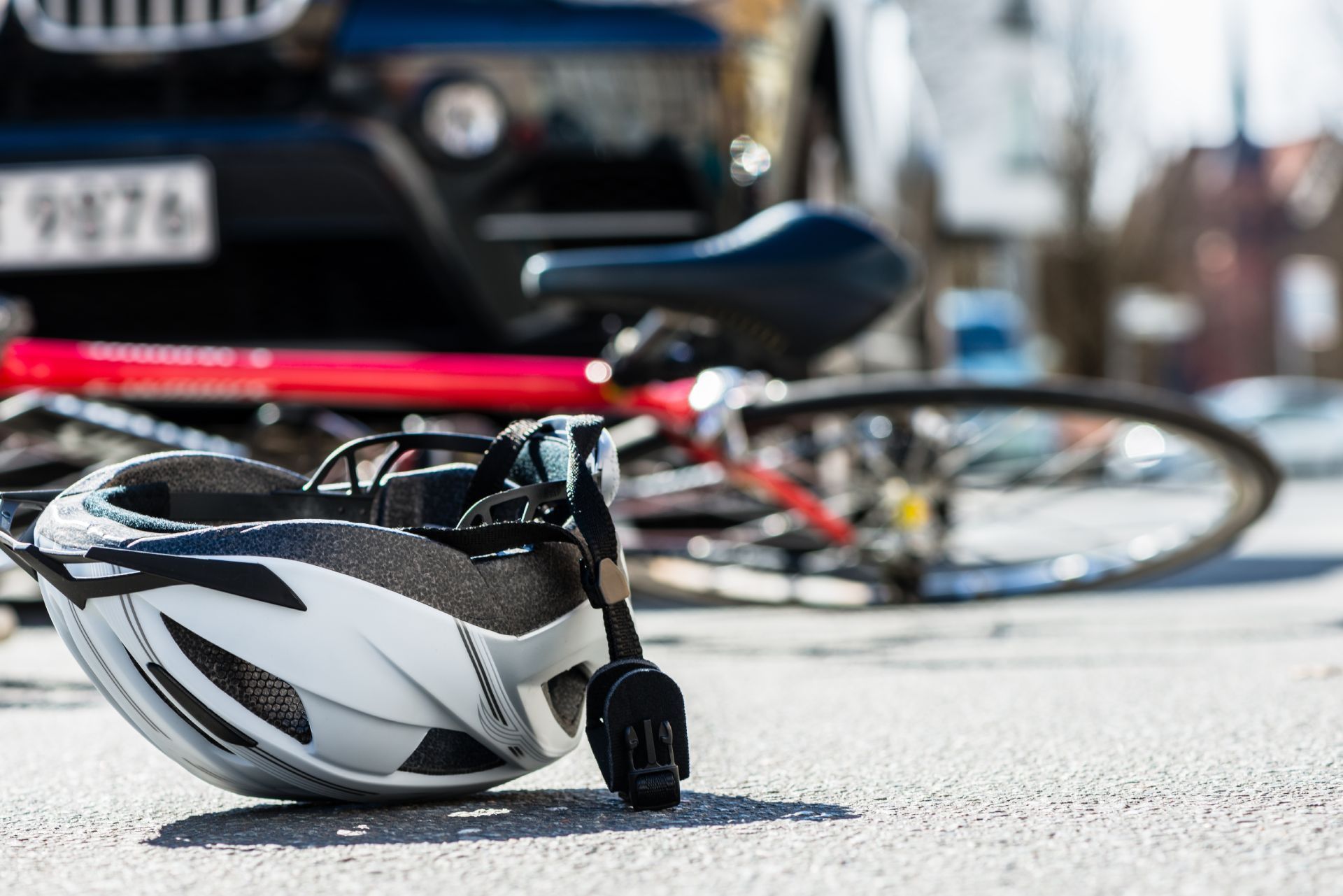Bike helmet on asphalt next to a fallen bicycle and a car, suggesting a collision.