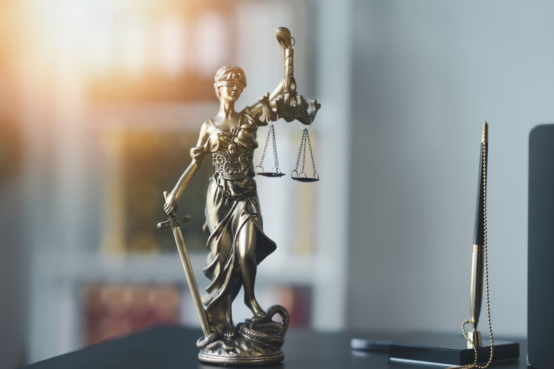 Golden statue of Lady Justice holding scales and sword, with a blurred background of an office.
