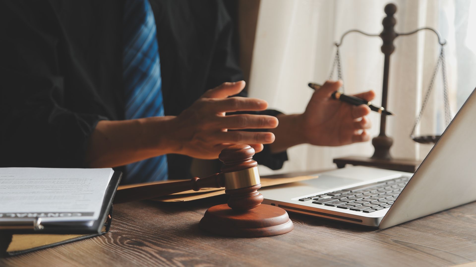 Person in suit with gavel and laptop, scales of justice in background.
