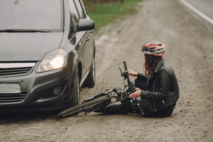 Car and cyclist after an accident. Cyclist wearing a helmet sits on the ground next to a bicycle and a car.