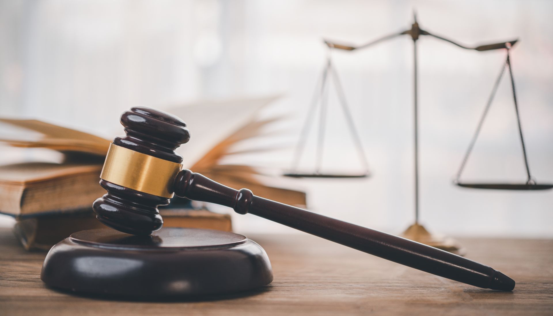 Gavel on wooden block, with scales of justice and open book in background.