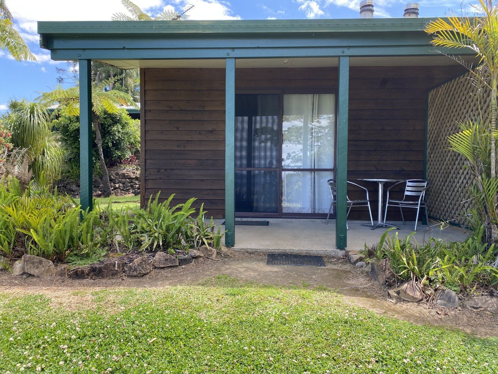 Cabin with a porch and furniture, surrounded by green grass and plants.