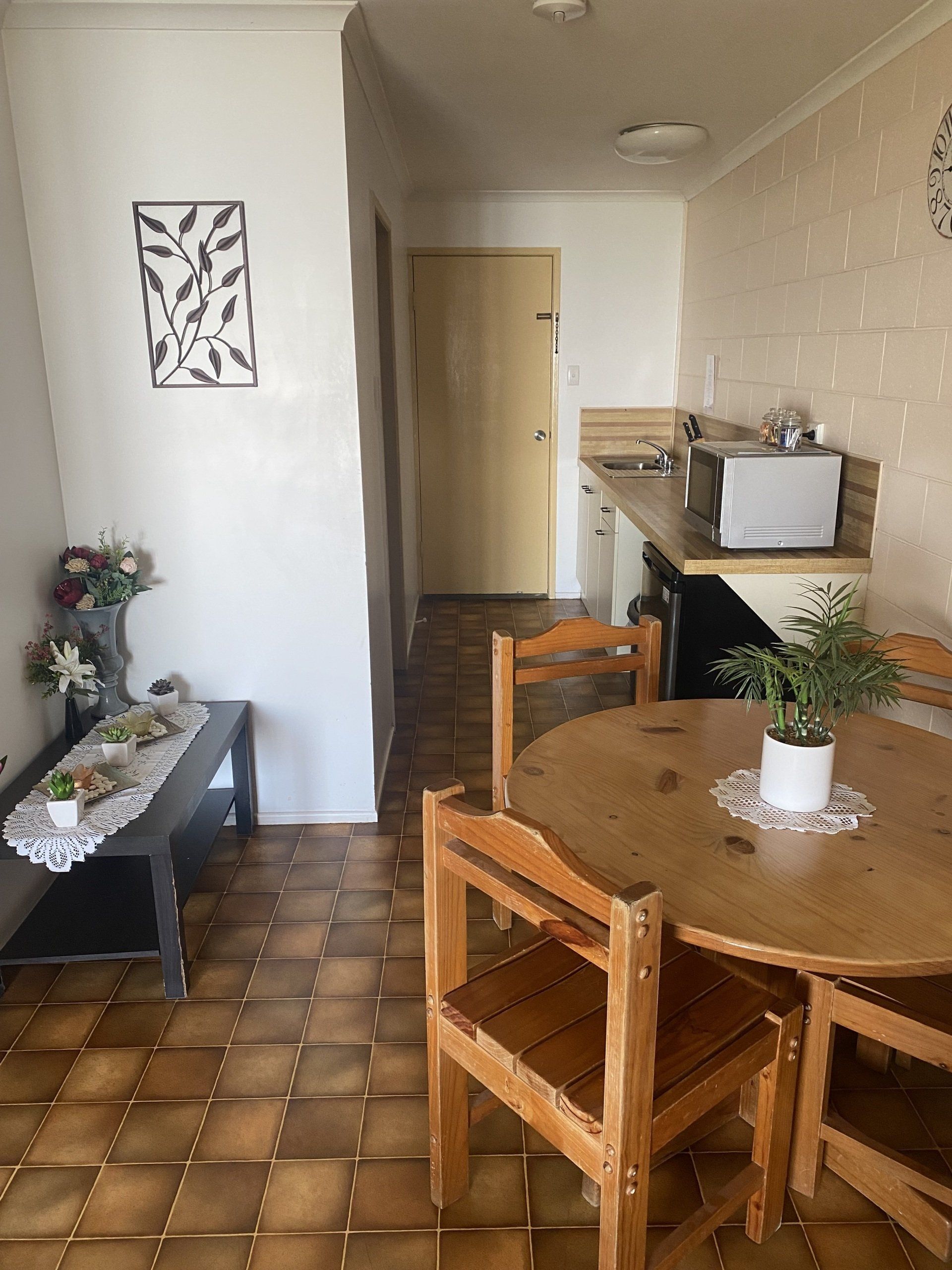 Interior view: dining table, chairs, kitchen counter with microwave. Tiled floor, art on wall, neutral colors.