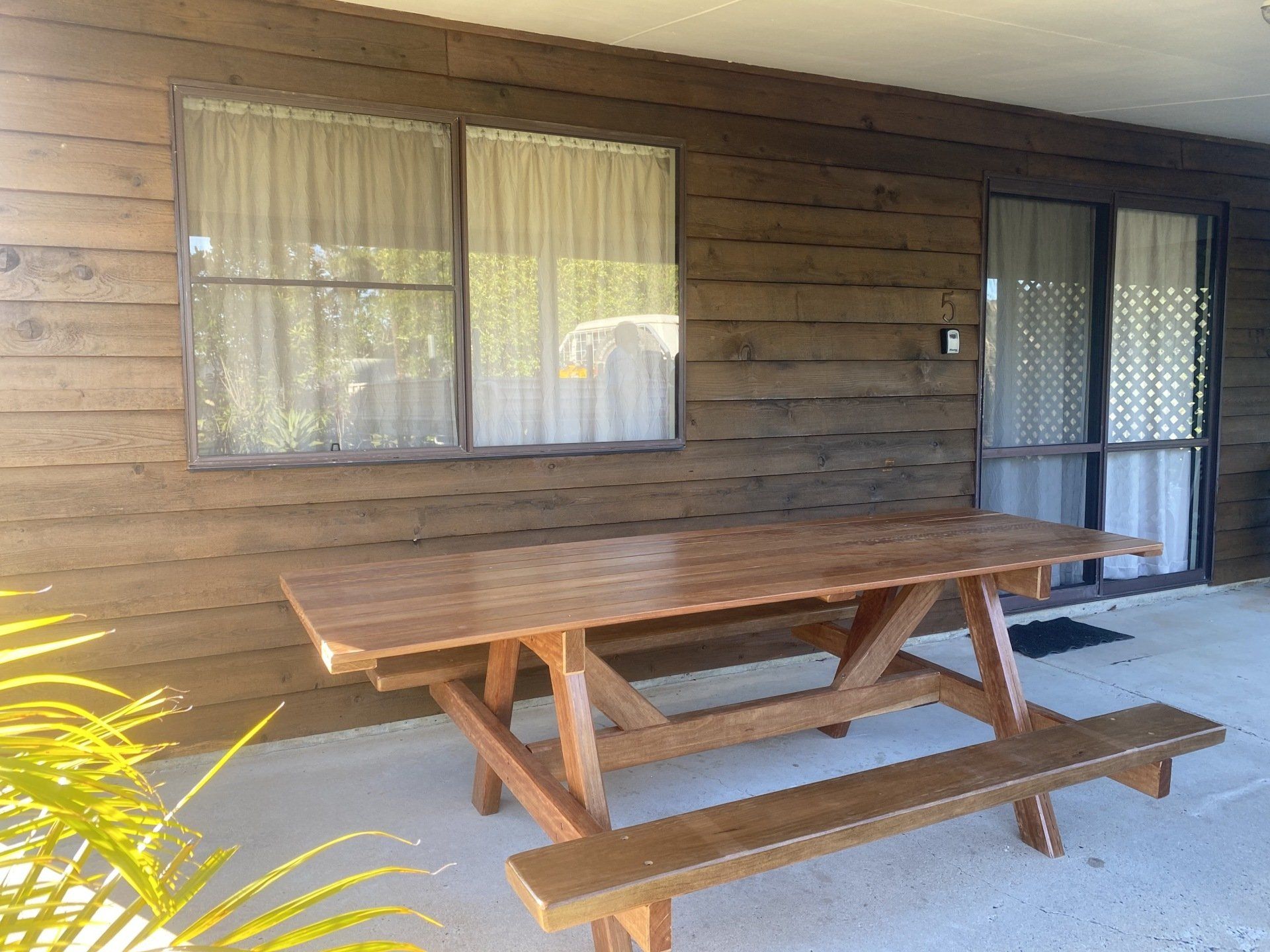 Picnic table on a porch with wooden siding, window with curtains, and a glass door.