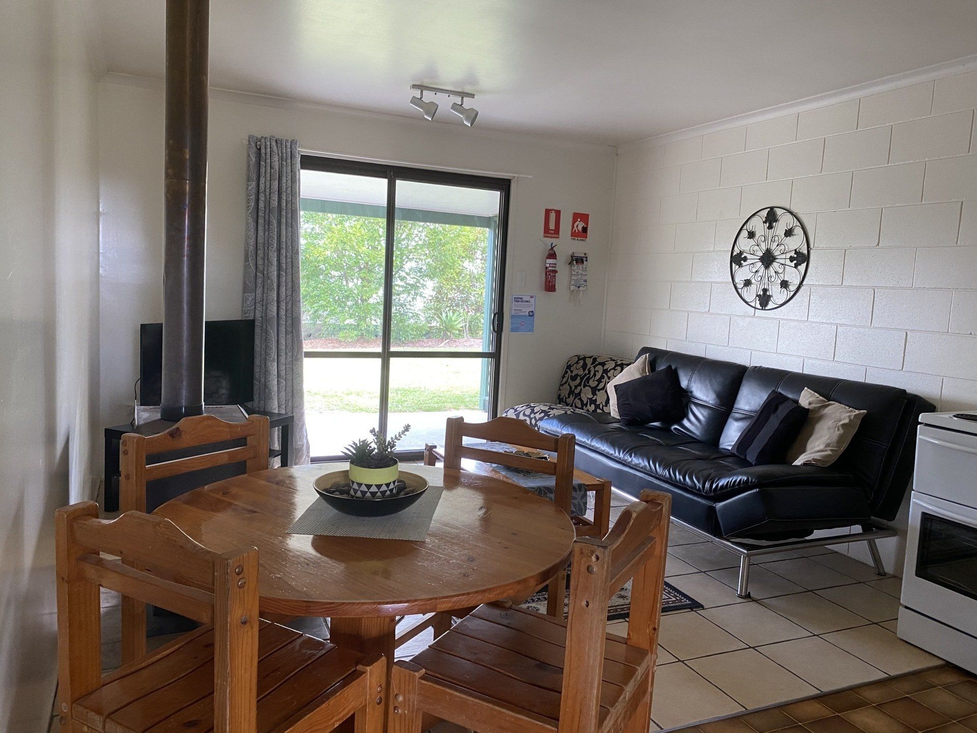 Living room with wooden dining table and black leather sofa. Large window and decorative wall art.