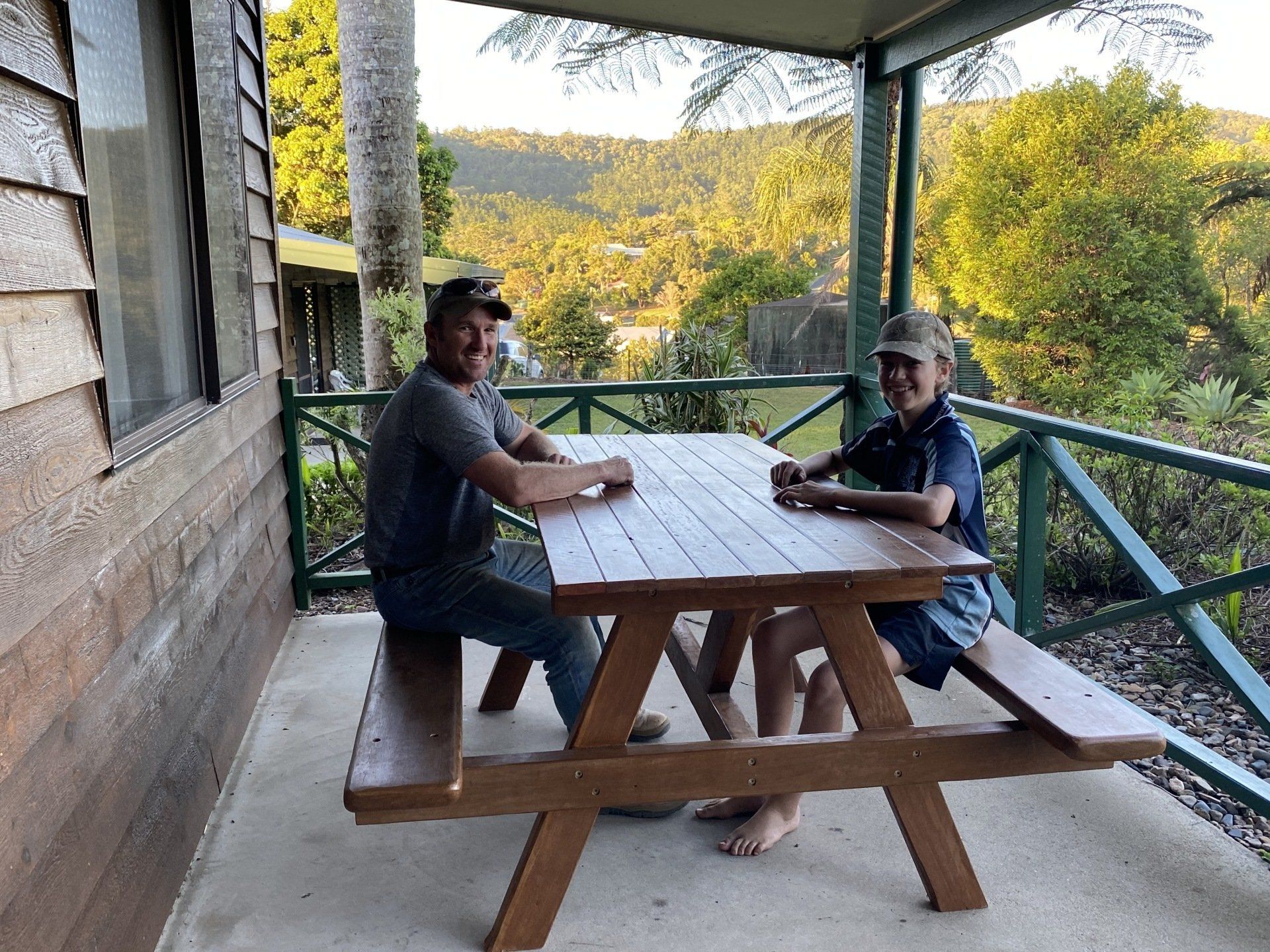 Two people seated at a picnic table on a porch overlooking a scenic landscape.