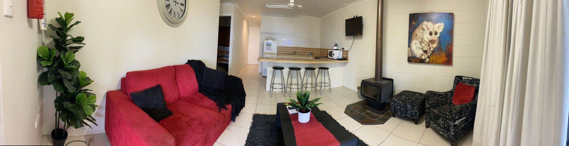 Living room with red sofa, black accents, kitchen bar, and fireplace. Decorative plant, art, and white curtains.