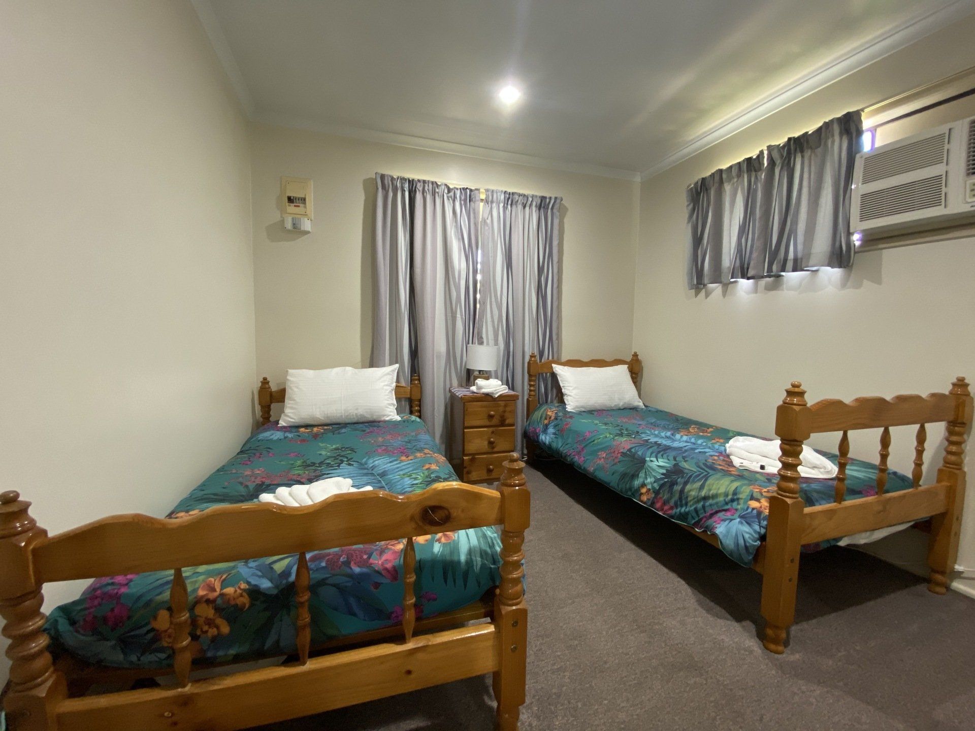 Two twin beds in a room with floral bedding, curtains, and an air conditioner.
