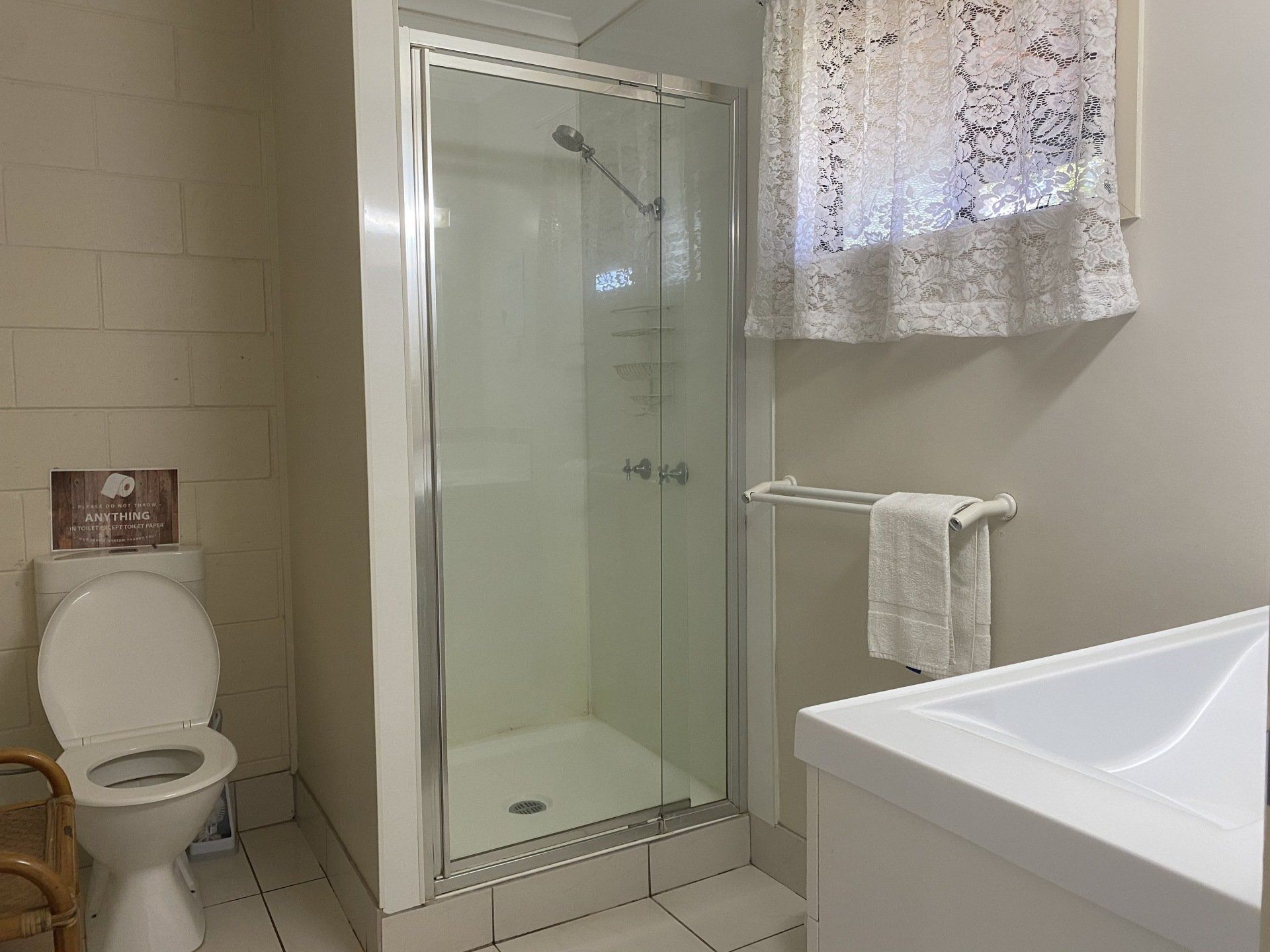 Bathroom with shower, toilet, and sink. White tiles and walls, with window.