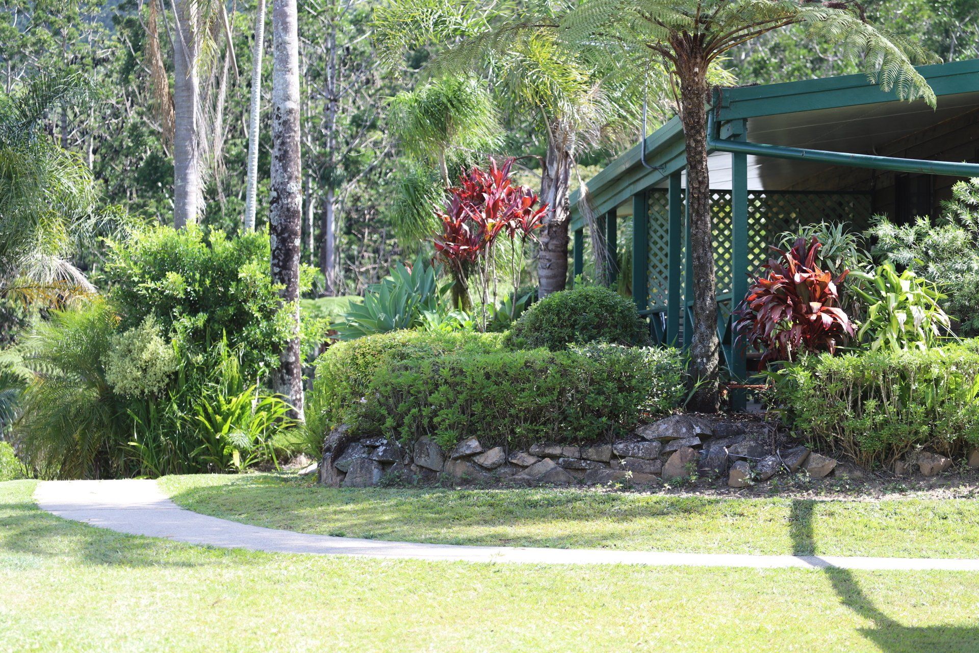 Green lawn with curved walkway, lush green garden beds, and building with porch.