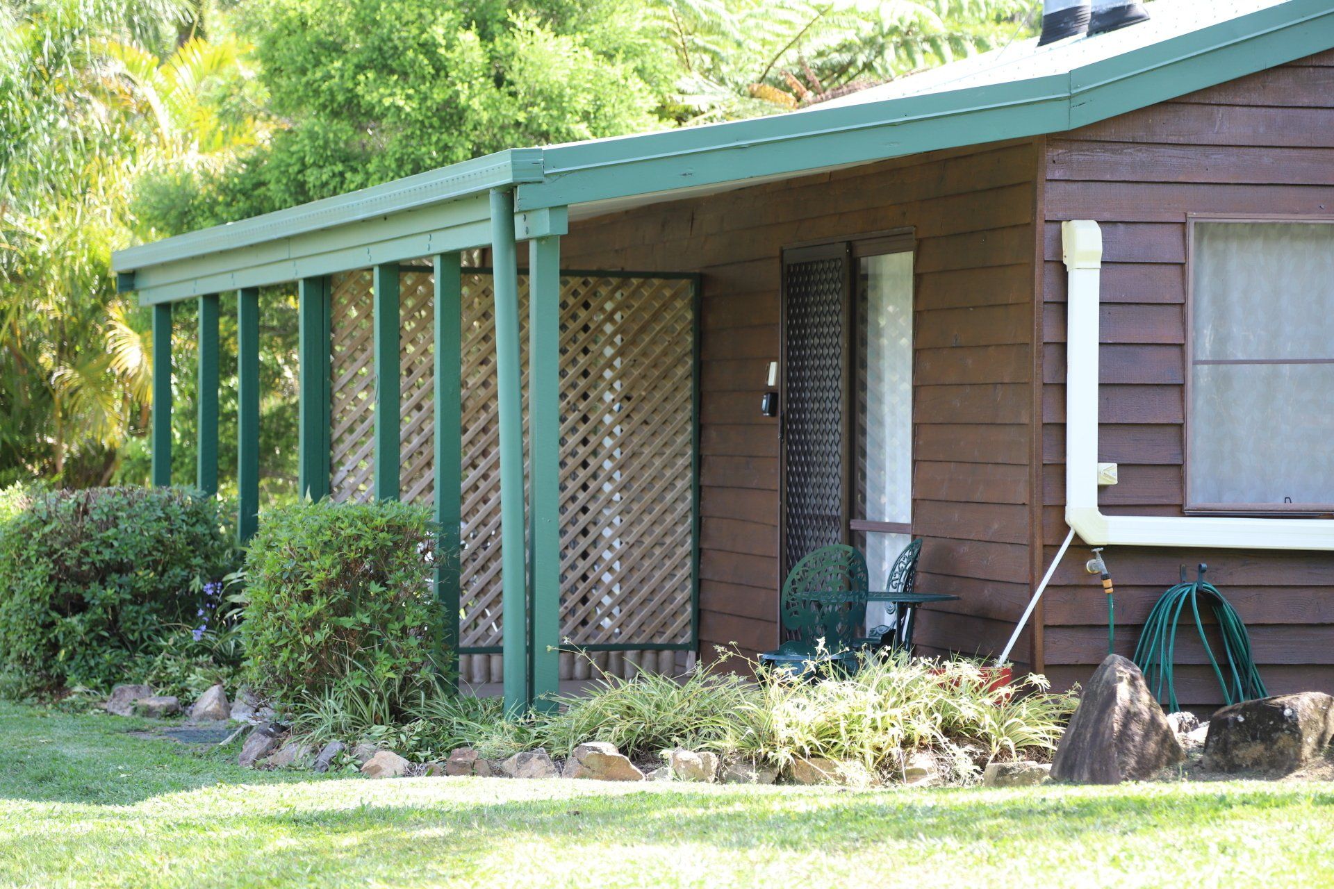Wooden Cabin with green trim and covered patio; a garden and lawn are in the foreground.
