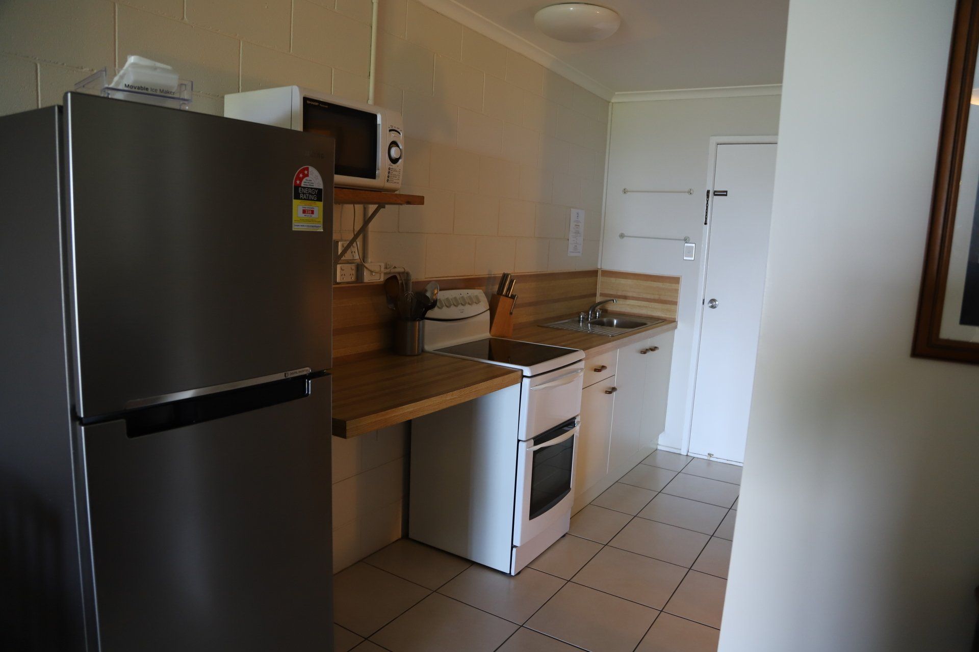 A small kitchen with a refrigerator, microwave, stove, and sink. White walls and cabinets.