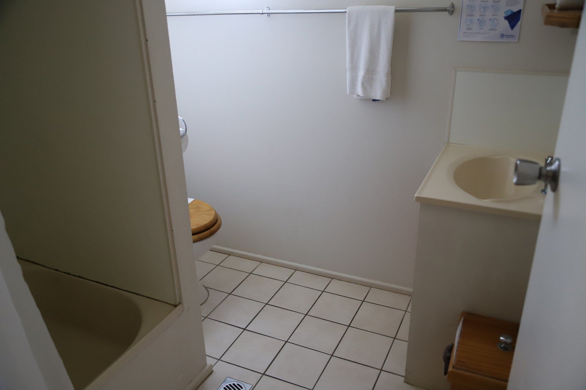 Small bathroom with bathtub, toilet, sink, and towel rack. White walls, tile floor.