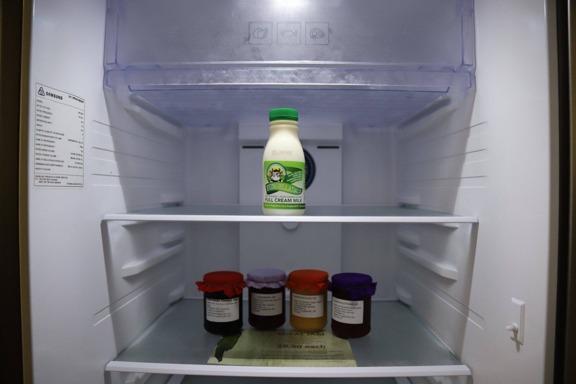 Inside a refrigerator: a bottle of milk and four jars of preserves.