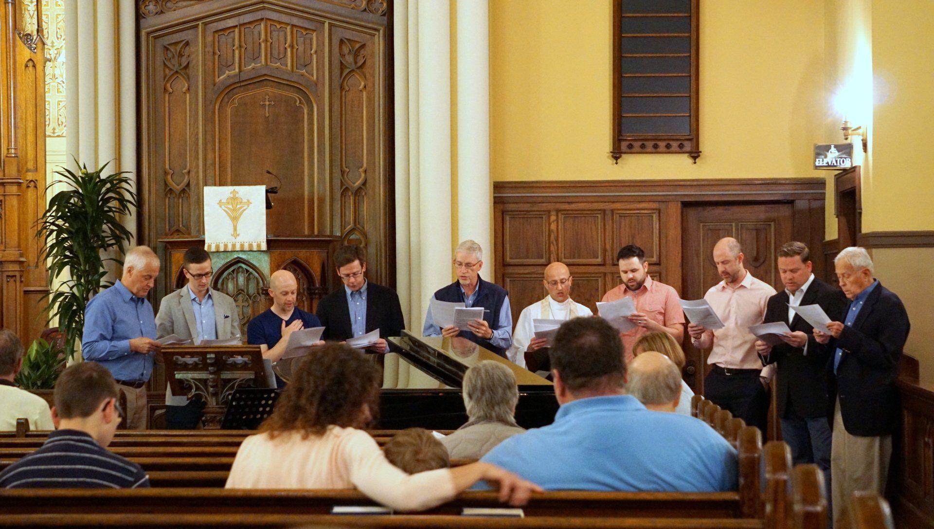 Choir singing in a church with wooden pews and altar. People hold sheet music.