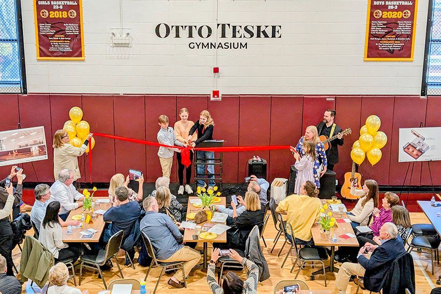 People celebrate at the Otto Teske Gymnasium ribbon-cutting. Balloons, tables, band, and red wall.
