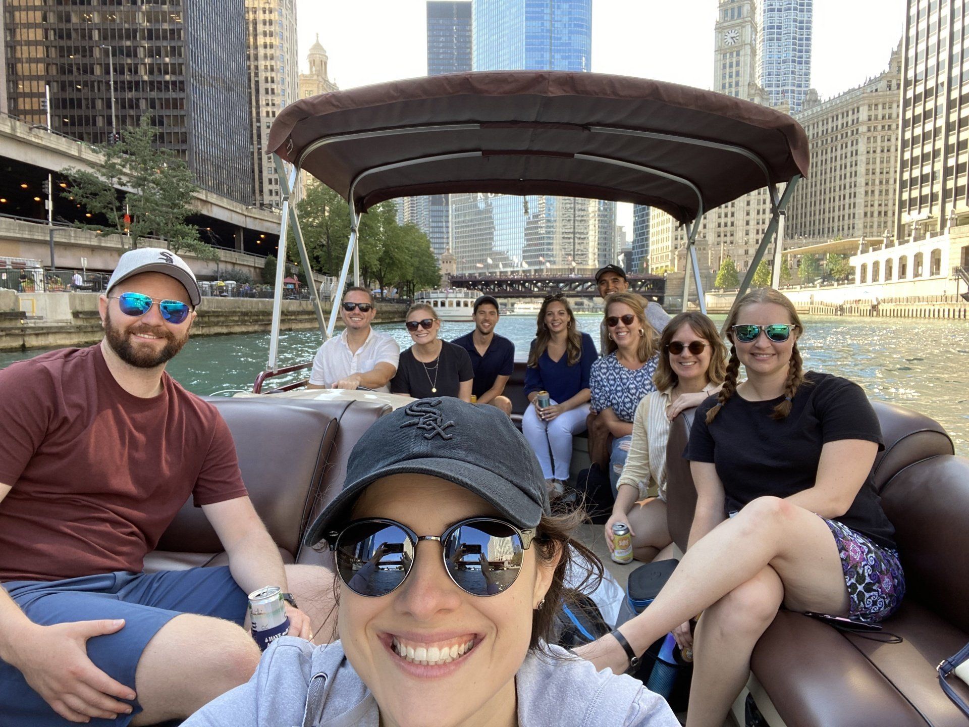 Group of people on a boat in Chicago, smiling at the camera. Tall buildings in the background.