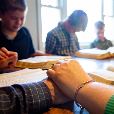 Students sit around a table with books open, studying together in a classroom.