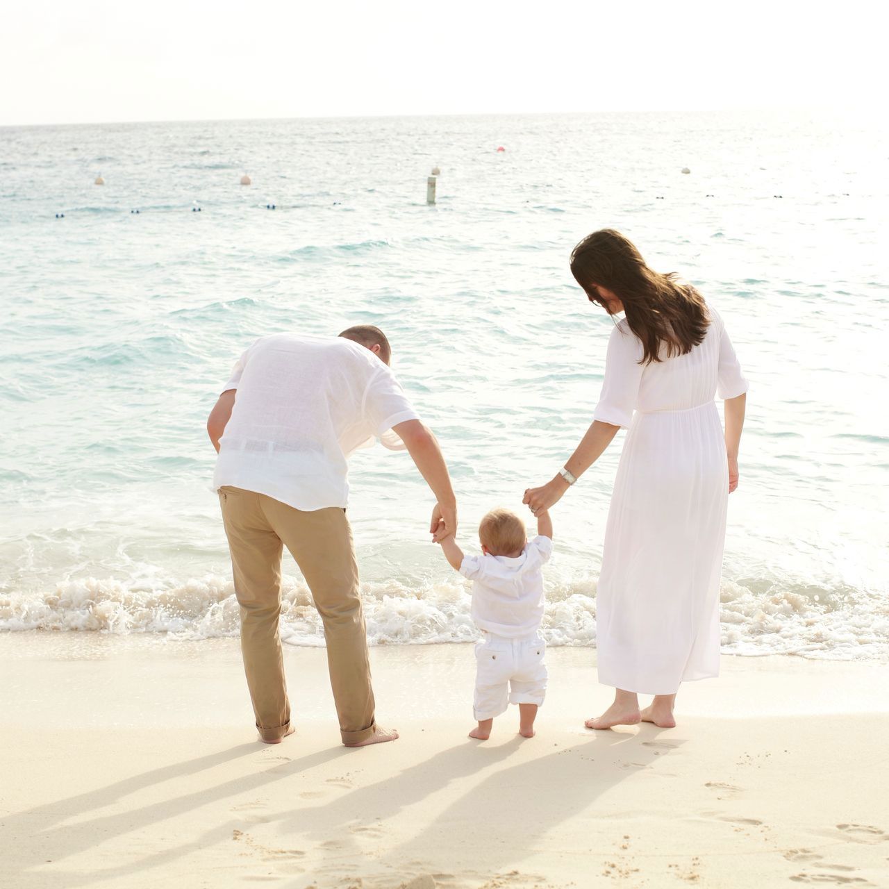 Family holding hands at the beach as waves lap the shore in bright sunlight