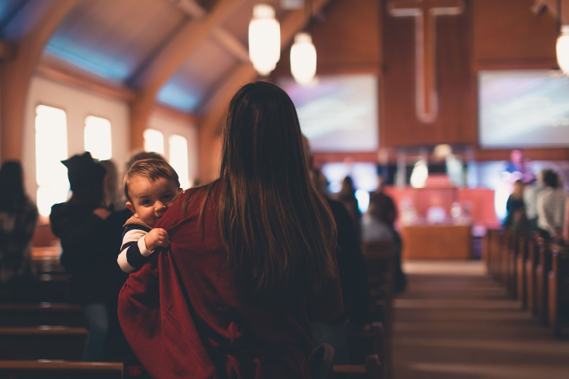 Adult holding a child in a church aisle during a service, with pews and warm lights in the background