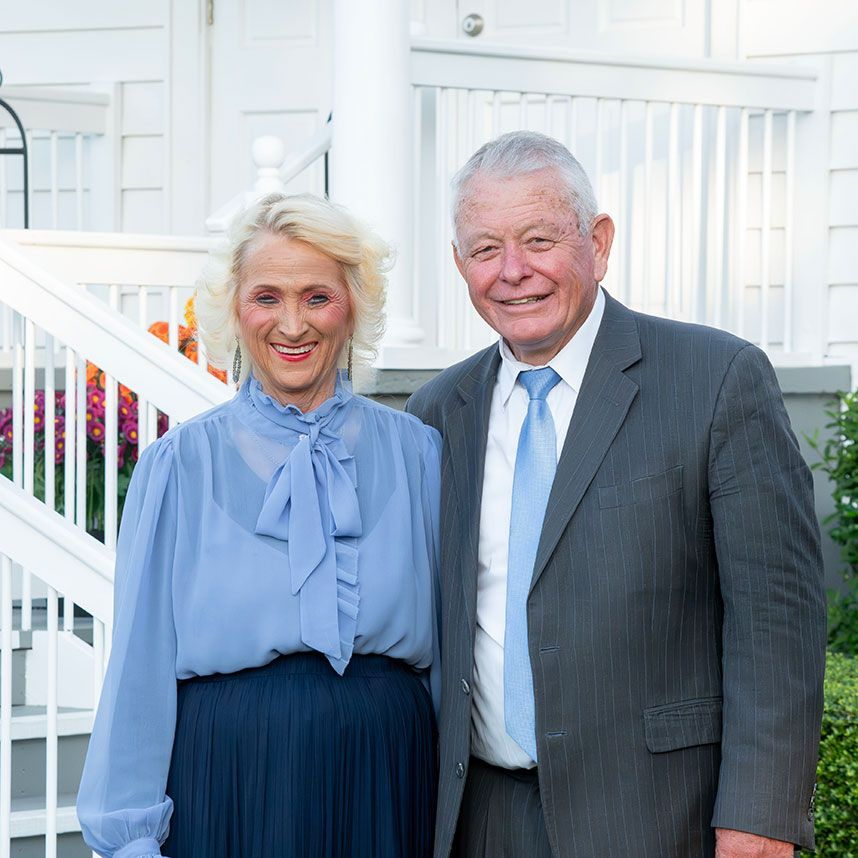 Two people in formal attire smiling outdoors in front of white stairs and railing