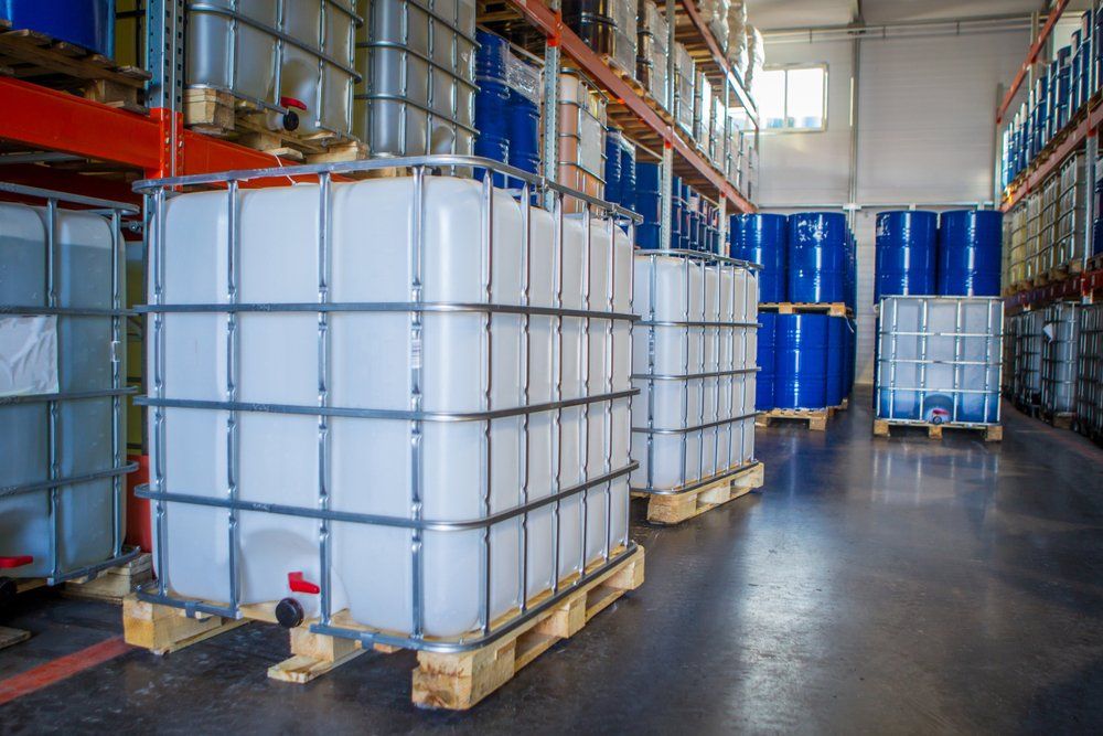 Entrepôt avec plusieurs grands réservoirs en plastique blanc et des barils bleus sur des étagères.