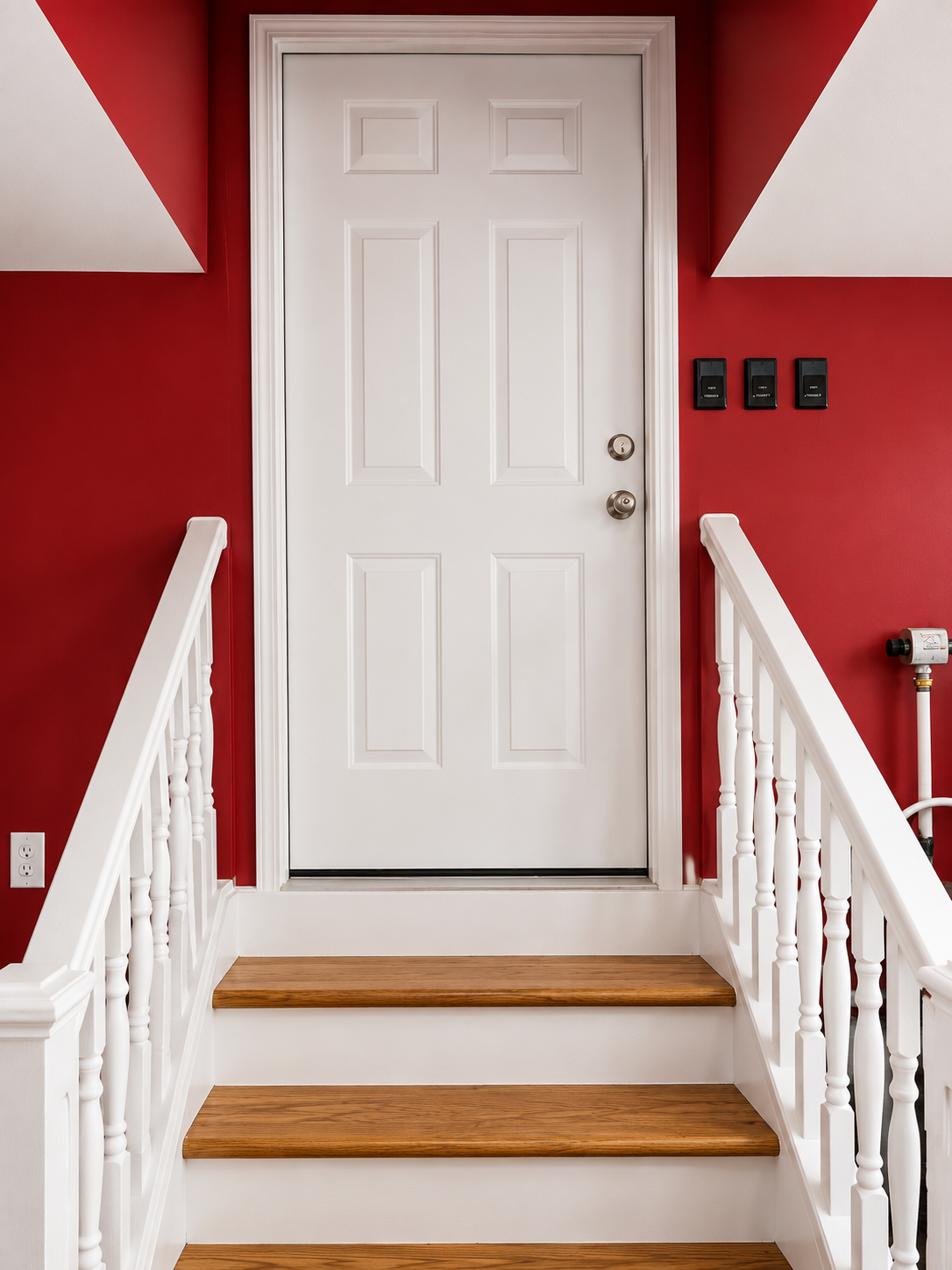 White front door at the top of short wooden steps, framed by red walls and white railings.