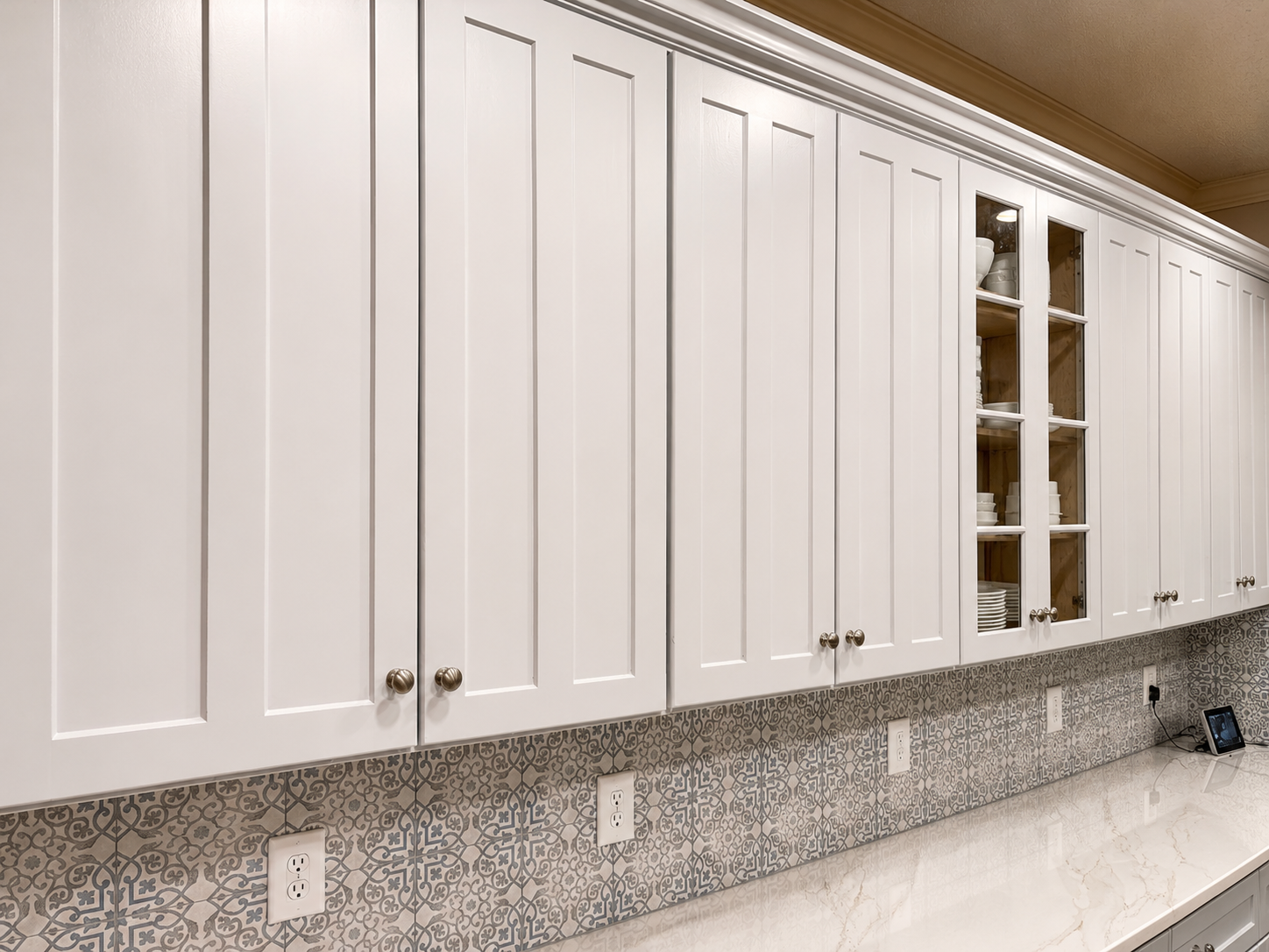 White kitchen cabinets with a glass-front cupboard and marble countertop backsplash line the wall.