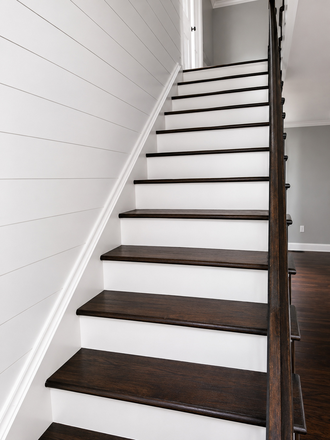 Staircase with dark wood treads, white risers, and a white wall in a bright hallway