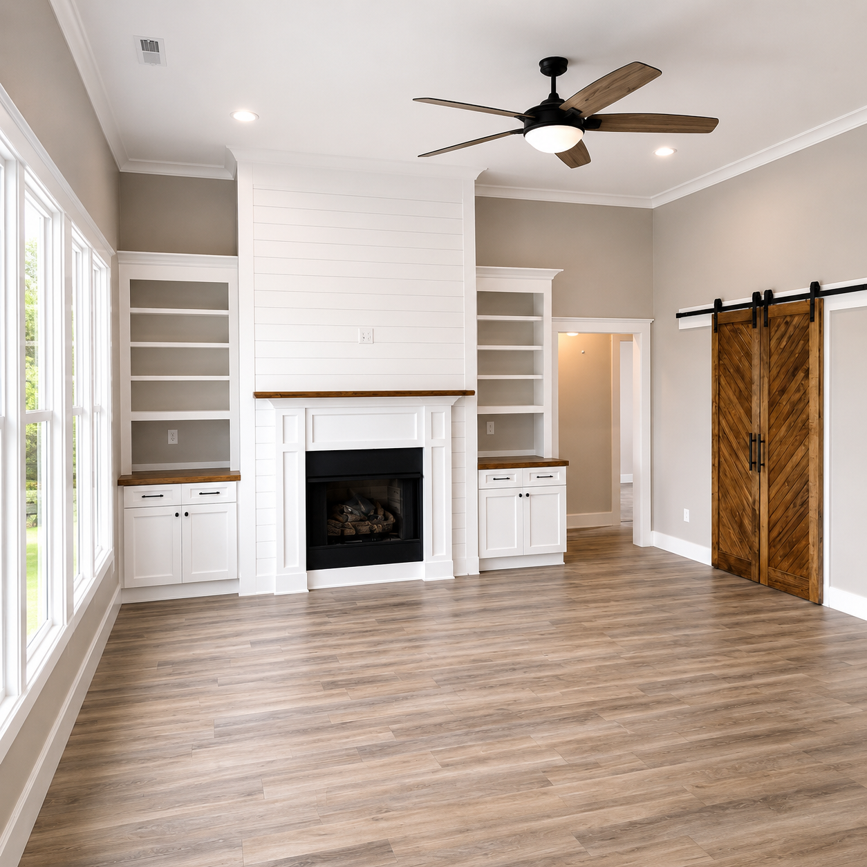 Bright empty living room with fireplace, built-in shelves, wood floor, and barn-style door.