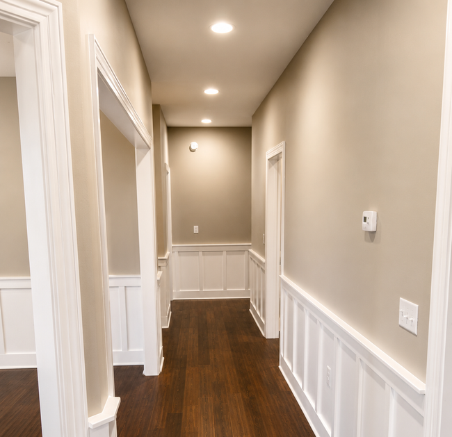 Narrow beige hallway with white wainscoting, dark wood floor, and recessed lighting