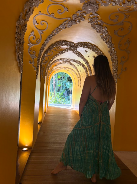 Mujer caminando a través de un túnel de arco dorado hacia una luminosa salida a un jardín.
