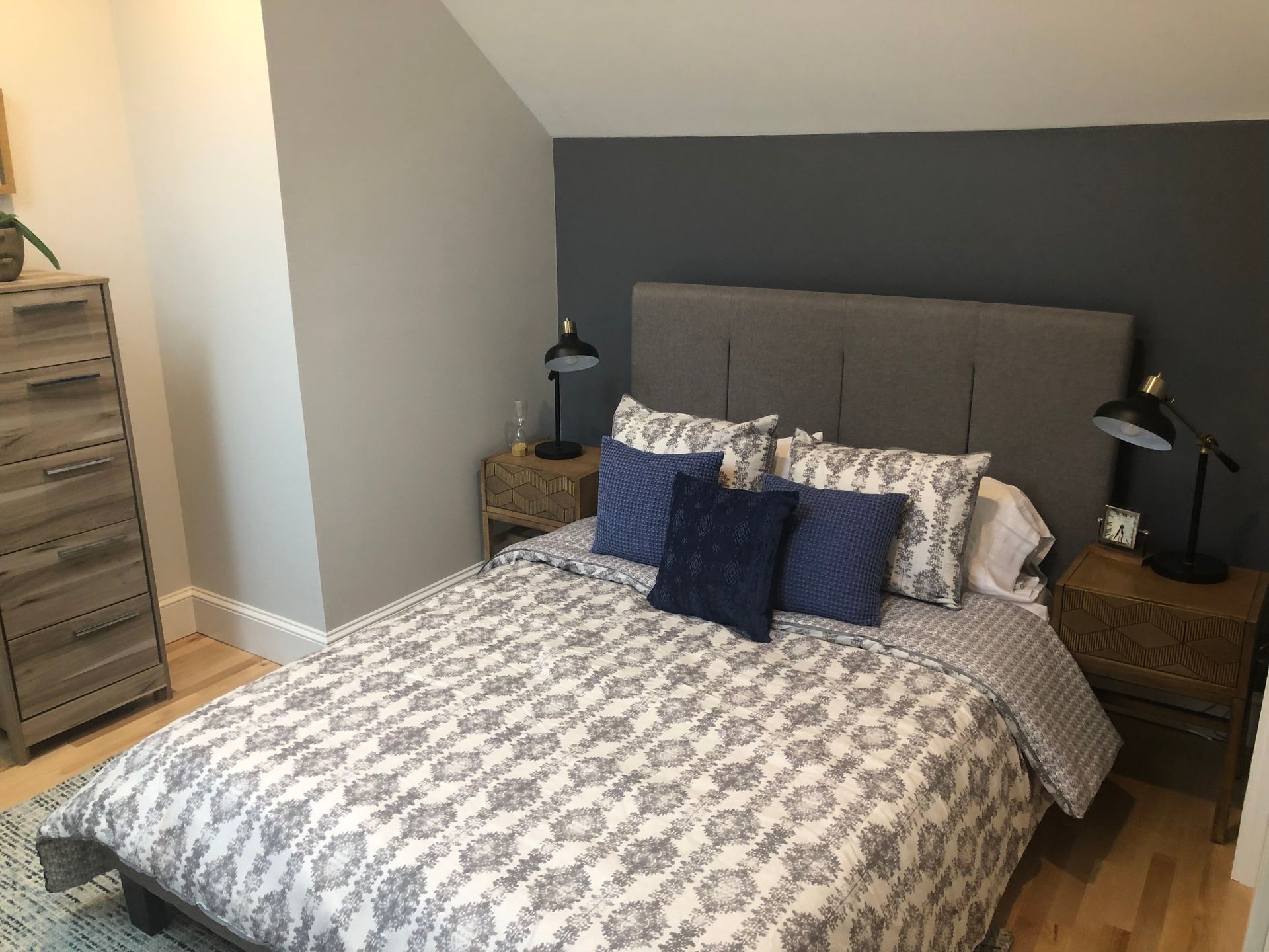 Bedroom with gray walls, bed with patterned comforter and pillows, nightstands, and a dresser.