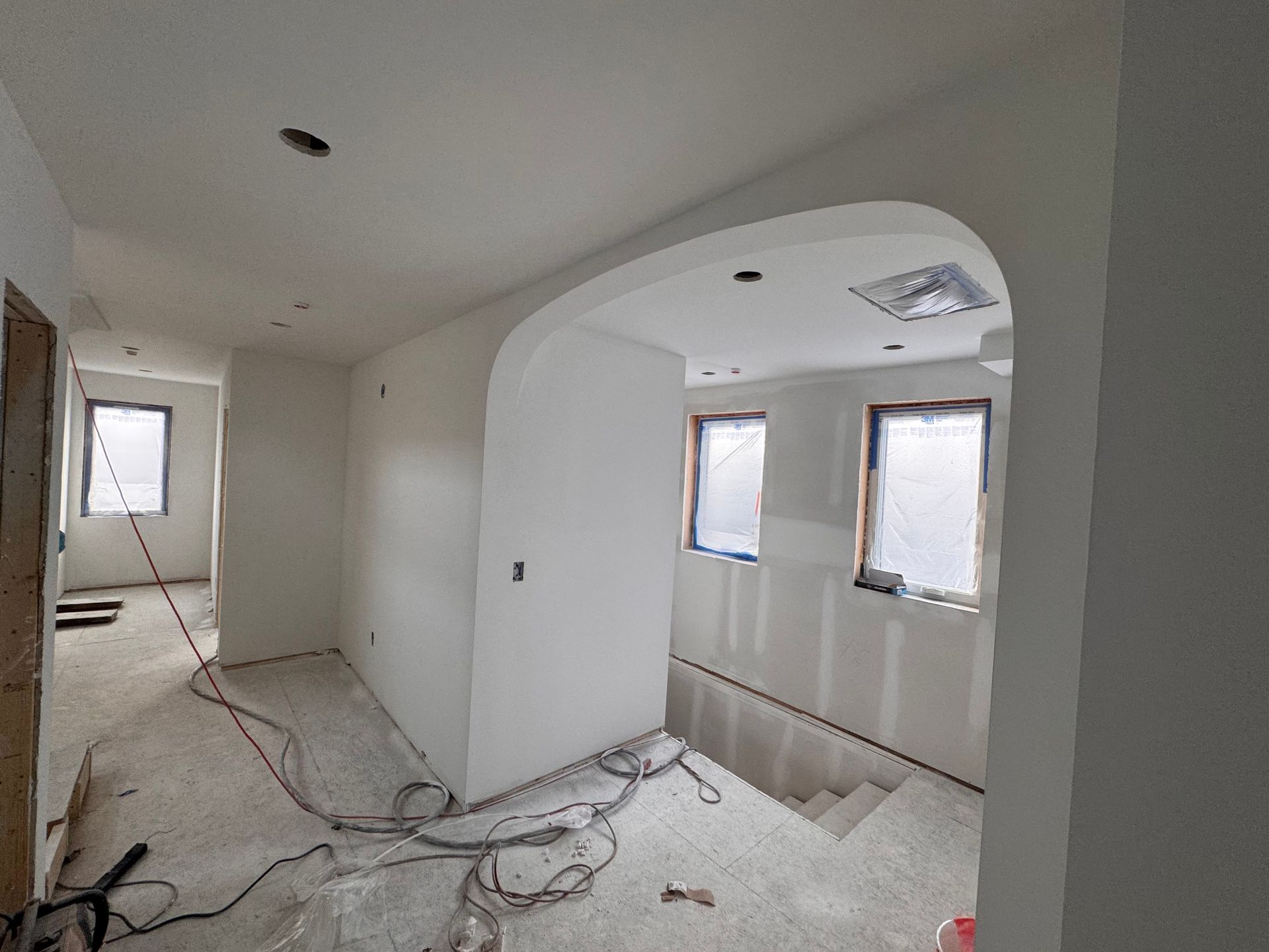 Interior of a building under construction, showing a hallway with arched doorway, drywall, and unfinished surfaces.