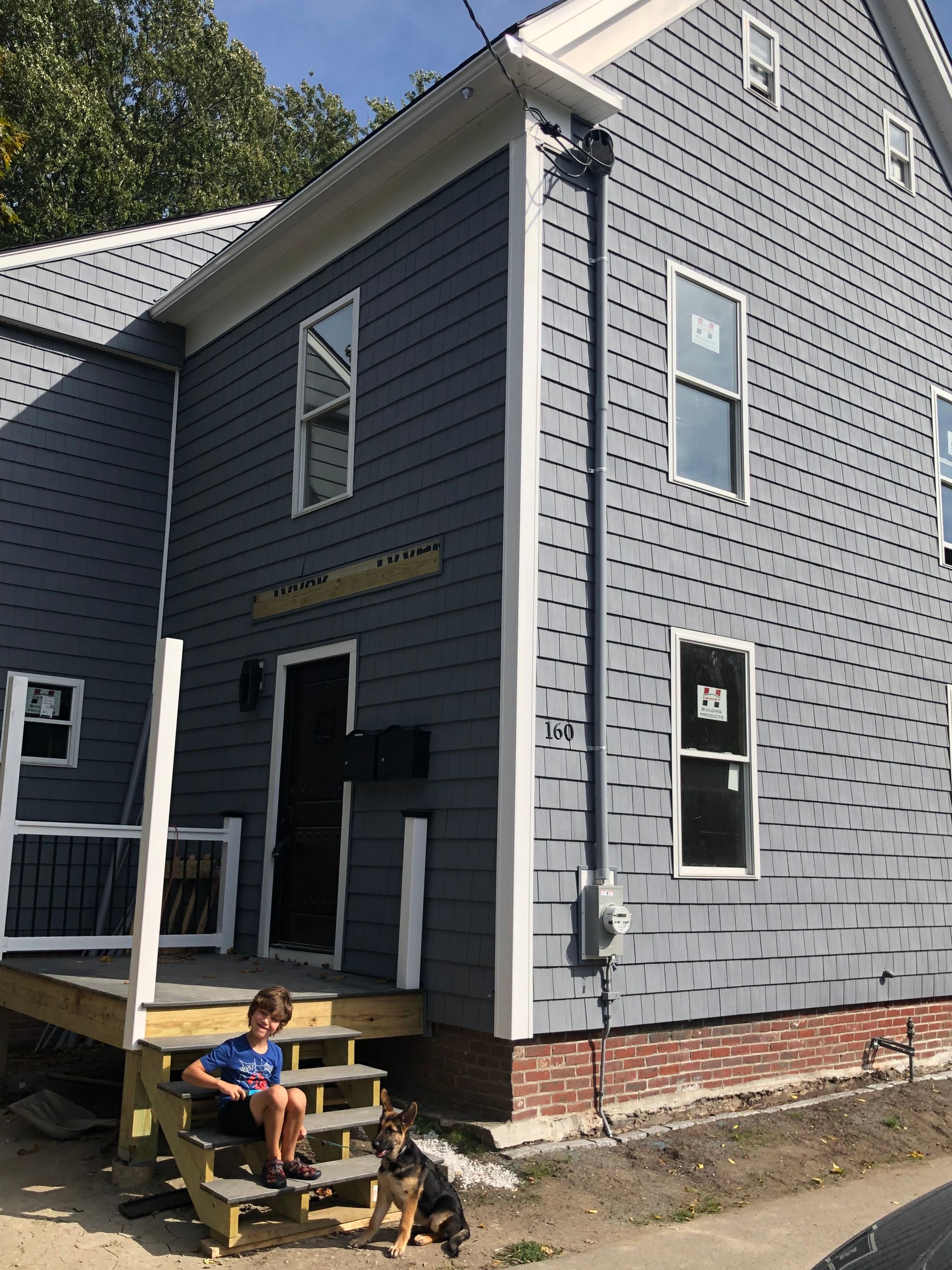 A two-story blue house with white trim. A boy sits on the porch steps with a dog.