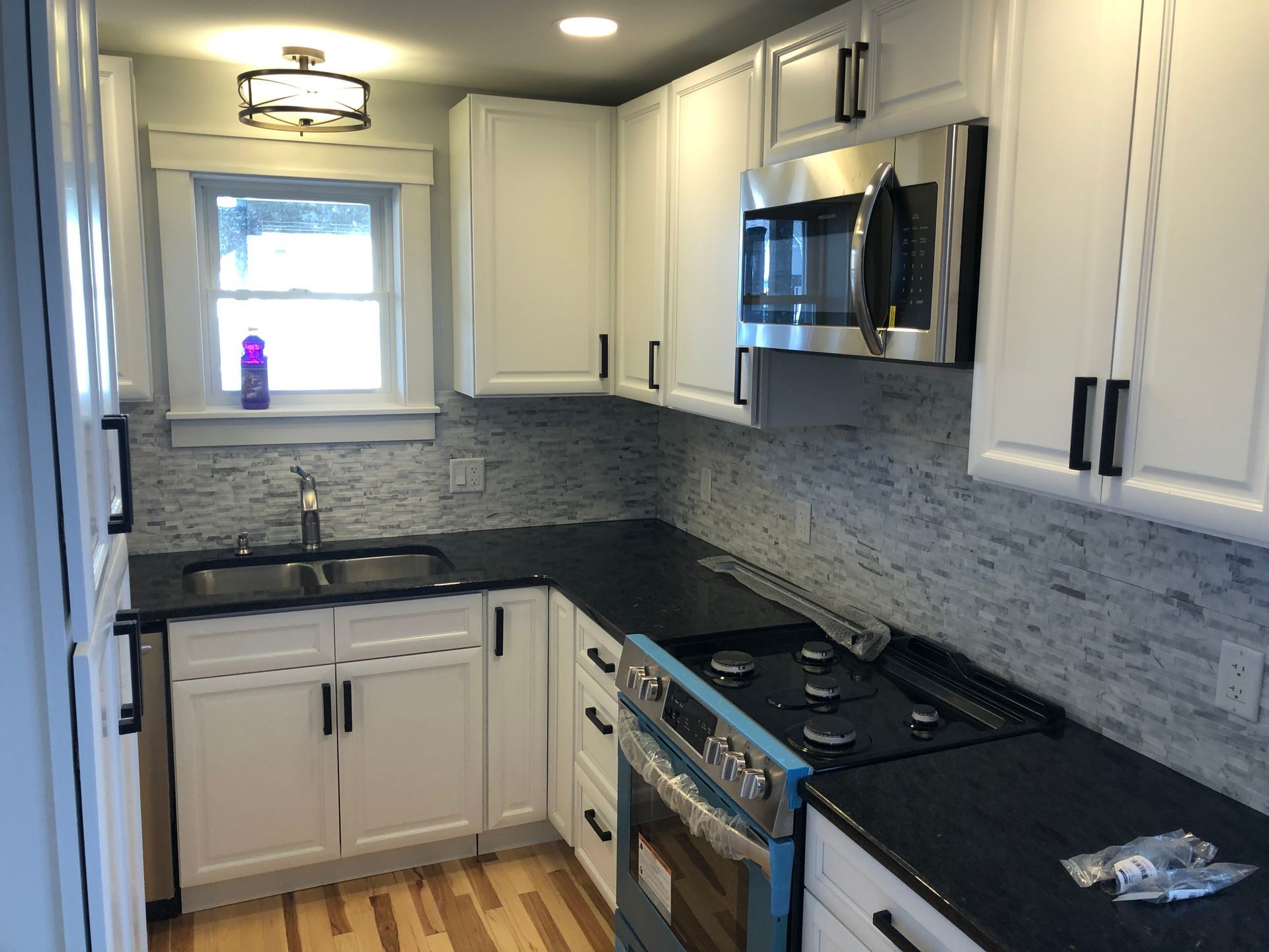 Small, modern kitchen with white cabinets, black countertops, and stainless steel appliances.
