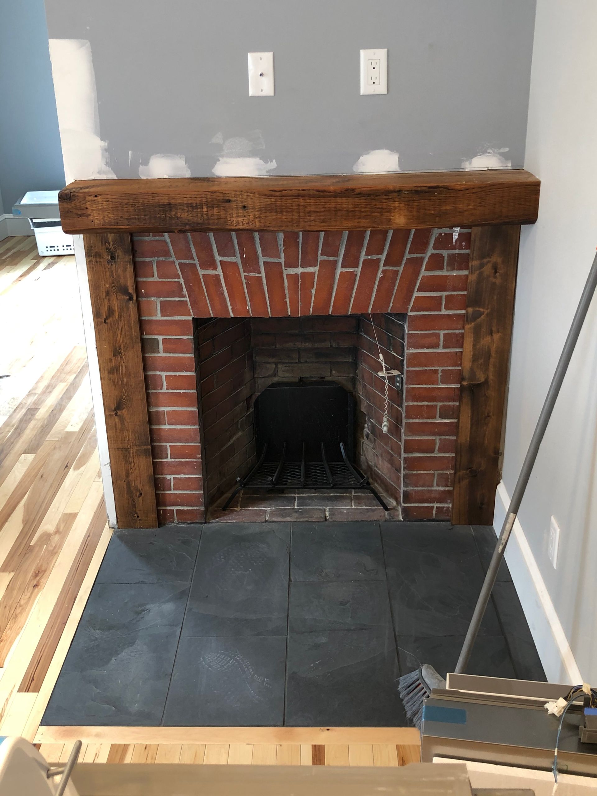 Brick fireplace with wooden mantel, gray hearth tiles, set in a room with hardwood floors and gray walls.