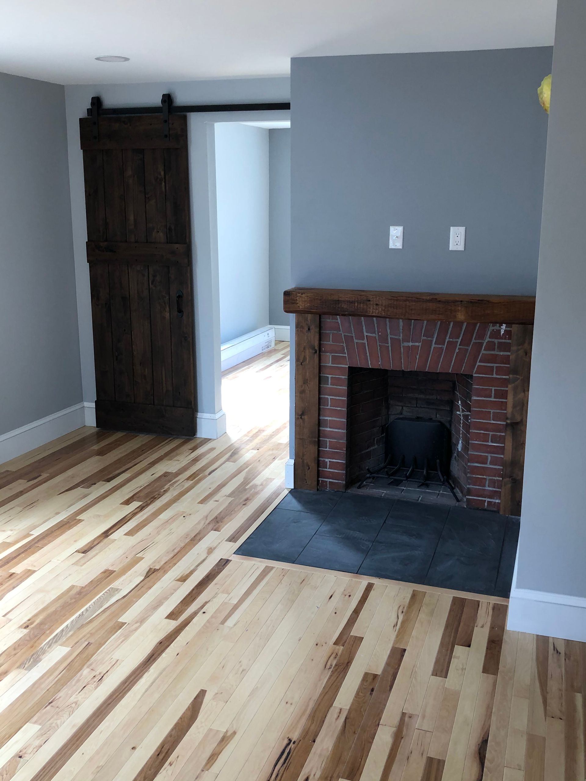 Room with hardwood floors, brick fireplace, wooden barn door, and gray walls.