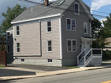 Two-story gray house with white trim and a small front porch, on a residential street.