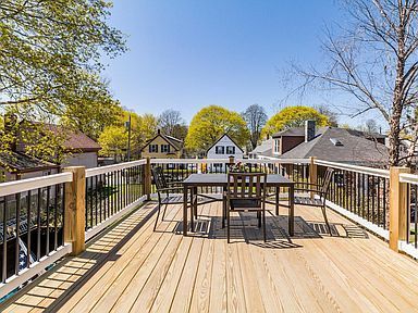 Wooden deck with table and chairs, overlooking neighborhood houses under a blue sky.