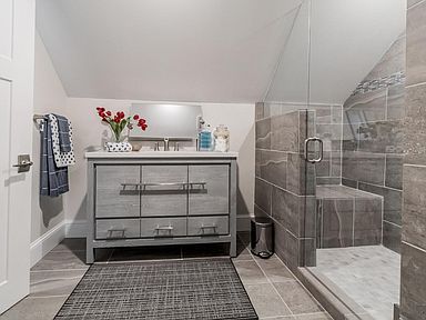 Gray bathroom with vanity, shower, and angled ceiling. Includes a door, towel rack, and rug.