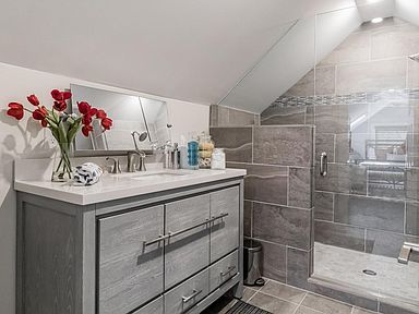 Gray bathroom with a sink, mirror, shower, and red tulips in a vase.