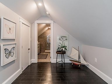 Attic space with sloped ceiling, hardwood floors, artwork, and an open doorway to a bathroom.