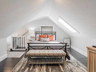 Bedroom with slanted ceiling; bed, bench, rug, small window, and steps to a platform with a gate.