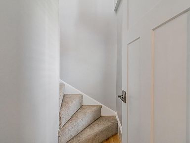 Staircase with carpeted steps next to a white wall and an open white door with a silver handle.