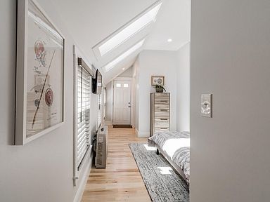 Narrow hallway with skylights, light wood floors, and a bedroom visible.