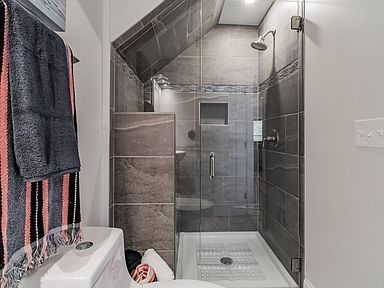 Bathroom with gray tile shower, glass door, white toilet, and towel rack.