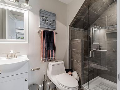 Small bathroom with gray tiled shower, white toilet, vanity, and a towel rack with towels.