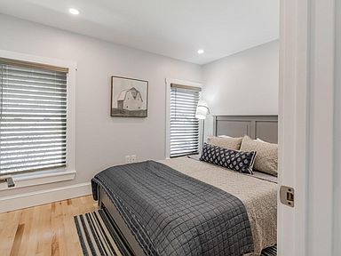 Bedroom with bed, windows with blinds, wood floor, gray walls.
